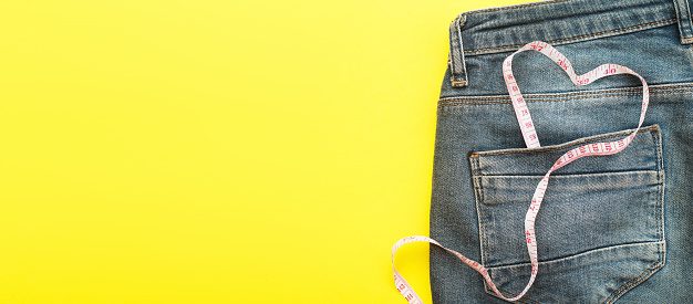 Close up of blue jeans with measure tape in the pocket in form of a heart. concept of a healthy lifestyle and diet with love to your body.banner