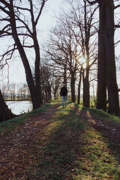 istock Young caucasian man with backpack stading on pond shore in spring tree tunnel at sunset. Czech landscape 1315218222