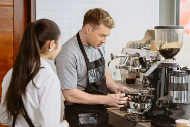 Photo of Professional Barista working in the cafe teaching make a coffee with espresso machine to new young staff