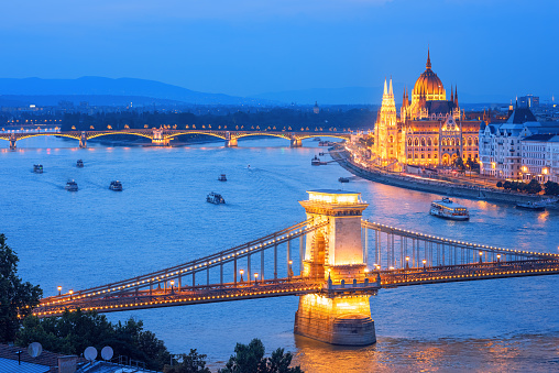 Budapest city, Hungary, the tourist boats cruising on Danube river along the Chain bridge and Parliament building on a blue evening