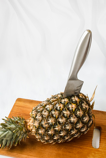 a knife stuck in a pineapple on a board on a white background.