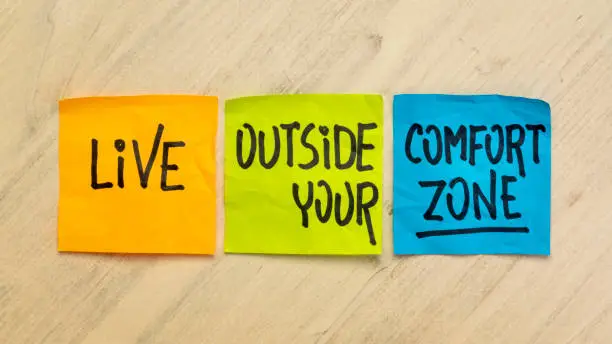 Live outside your comfort zone - motivational handwriting in black ink on sticky notes against distressed  wood, challenge and personal development concept