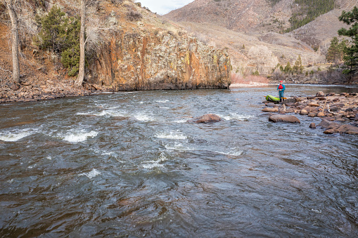 kayaker with a whitewater inflatable kayak on a shore of mountain river in early spring - Poudre River in northern Colorado, low angle aerial view