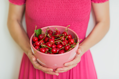 Closeup cherry berries in a pink bowl at female hands. Gardening, agriculture, harvest and forest concept.