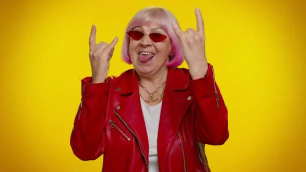 Overjoyed elderly granny woman rocker showing rock n roll gesture by hands, cool sign, shouting yeah with crazy expression, dancing, emotionally rejoicing in success. Senior mature old grandmother