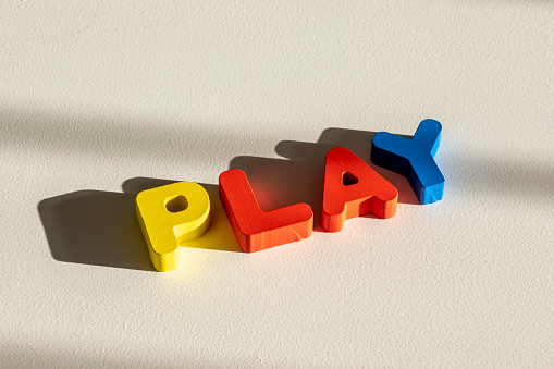 Meaningful words with single letters concept: Colorful collection of wooden ABC learning toy letters. White background. Light coming from an angle and creating long shadows. Creative design with copy space