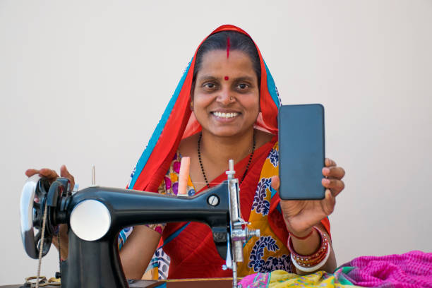 indian rural woman using sewing machine and showing her mobile phone - day asian ethnicity asian culture asian and indian ethnicities imagens e fotografias de stock