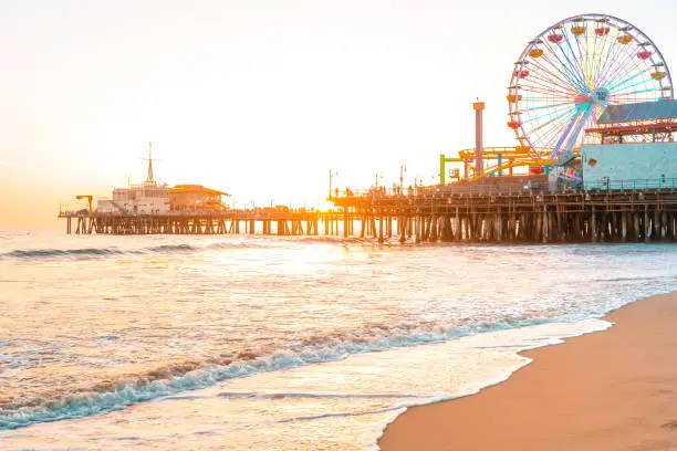 Photo of Santa Monica Pier on the background of an orange sunset, calm ocean waves, Los Angeles, California