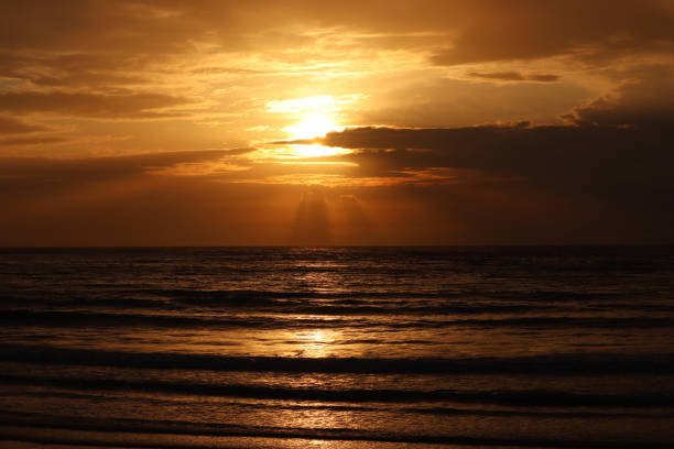 istock Sunset on a beach, orange sun is shining through the clouds and reflected in dark waves 1315239928