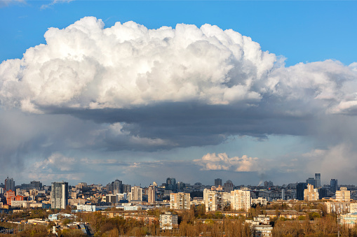 A beautiful spring cityscape with a white cloud hovering over the city in the blue sky under the sunbeams.