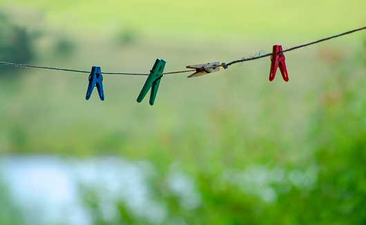 Colorful clothespin clothespins on the rope. Colourful cloth clips in a blue rope waiting for the next batch of clothes to come after laundry. Clothespins on a rope against a blurred natural background