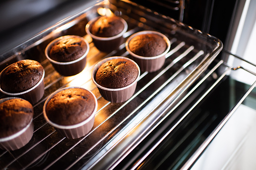 Open home oven with chocolate tasty muffins in bakeing forms on tray at home. Making fresh cupcakes in stove close up.