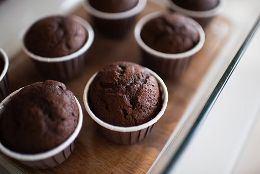 Fresh baked chocolate muffins in forms at kitchen table close up. Healthy eating. Cooking at home.