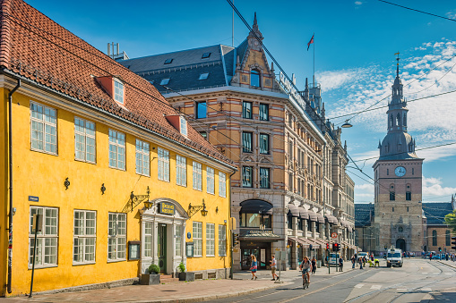 People walk and bike on Grensen street in Old Town Oslo, Norway on a sunny day. The Oslo Cathedral is in the background.