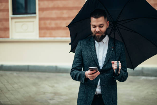 istock Businessman using a smartphone and holding a black umbrella 1315259726