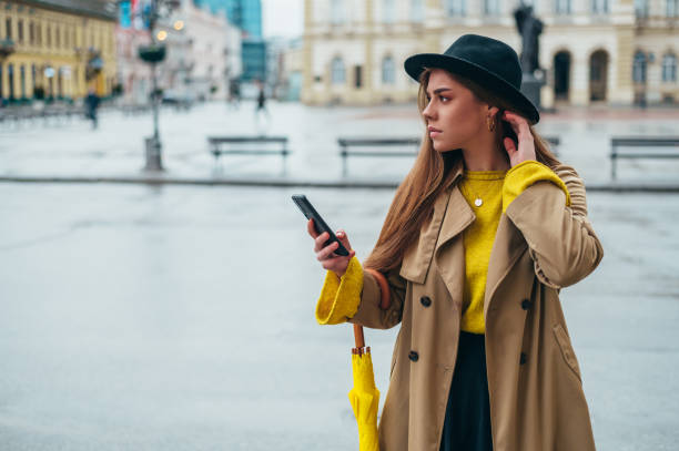 istock Woman using a smartphone and holding a yellow umbrella outside 1315259731