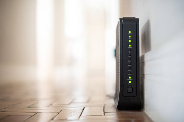 Wi-Fi Router Router - Wifi Modem, with flashing lights, on the floor, near the corner of a wall in a well-lit house. router stock pictures, royalty-free photos & images