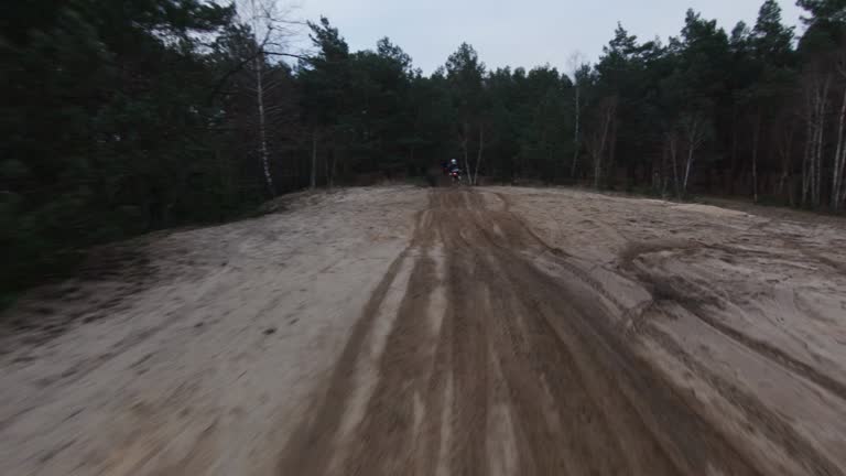Motocross race at dusk. Drivers speeding on cross country terrain. FPV - Racing drone view. Passing by drivers