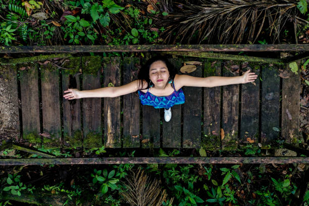 a young womand standing on a wooden bridge inside a forest looking up at the camera with her arms strechted out to enjoy the pure air of nature - 3144 imagens e fotografias de stock