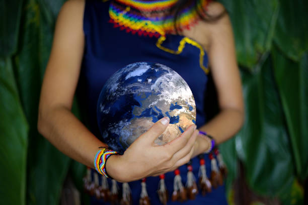 an indigenous female in traditional clothing holding the earth with two hands close to her belly - native habitat imagens e fotografias de stock