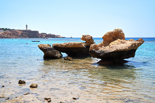 Rocks on beach, rocky coast of popular resort area Hadaba bay, blue sky and water. Unknown people are swimming in Red Sea, Sharm Al-Sheikh, Egypt