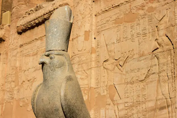 Horus statue in the courtyard of the Temple of Edfu with hieroglyphics on wall, Edfu, Egypt