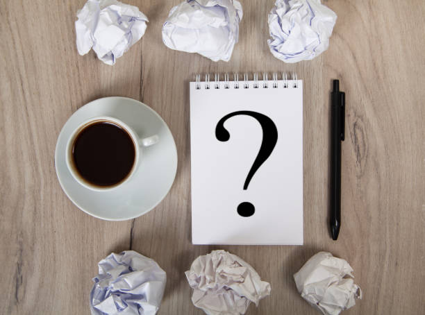 istock Notebook with question mark, coffee, black pen and crumpled papers. Light colored wooden background. 1315293733