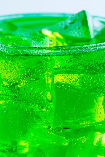 A glass of green cold drink with ice cubes.