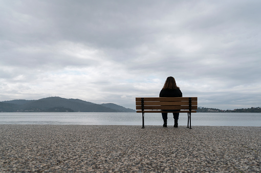 Overweight young woman sitting on a bench by the sea watching the view
