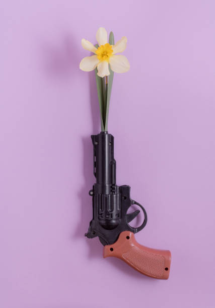 Plastic revolver with a yellow narcissus in the barrel. Creative spring concept.