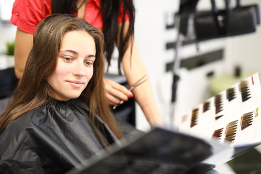 Woman in beauty salon chooses hair dye color from catalog. Hair coloring and right shade of the concept