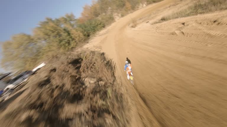 Motocross race. Driver speeding on cross country terrain. FPV - Racing drone view. Following driver