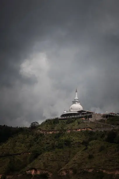 Mahamevnawa Buddhist Monastery temple in the mountain top low angle scenic landscape view. dark rainy clouds and cold atmosphere in Bandarawela, stupa glowing brightly in the distant hill.