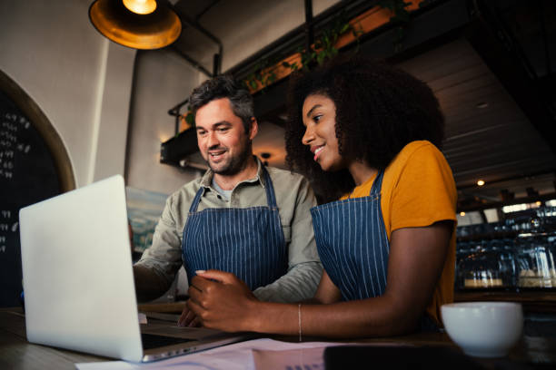 istock Manager of coffee shop training intern showing menu on laptop while drinking hot coffee in cafe 1315333132