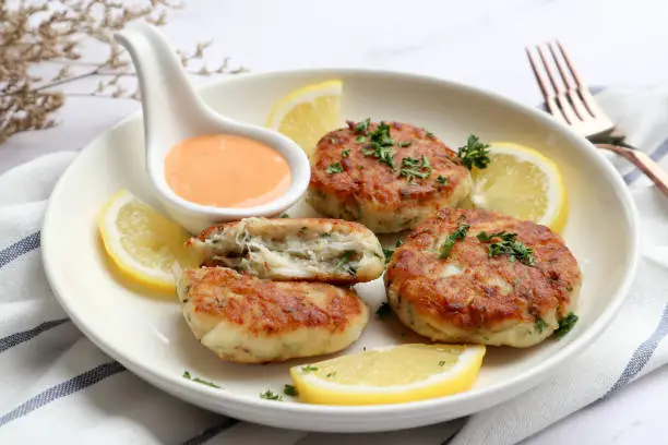 Photo of Crab cake with remoulade sauce and lemon in a white plate on the marble tale - close up view