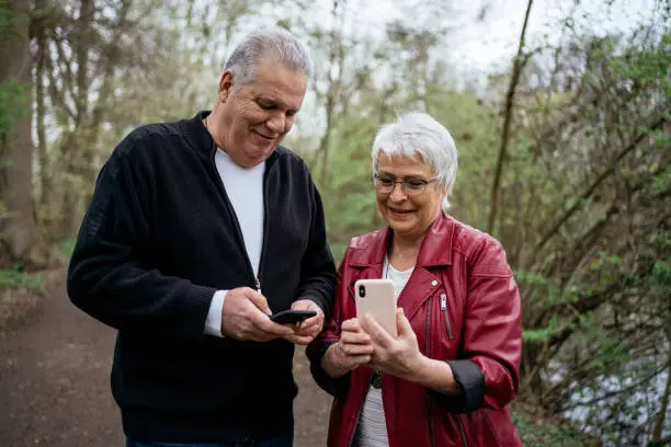 Elderly couple standing in nature and using their smart phones