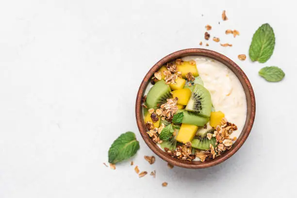 Mango yogurt with granola and kiwi in wooden bowl on white background. Healthy dairy product breakfast