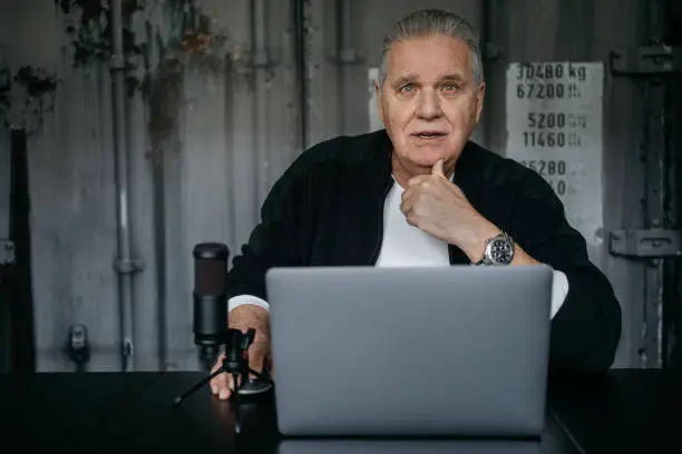 Elderly man working on a laptop with a microphone during video conference