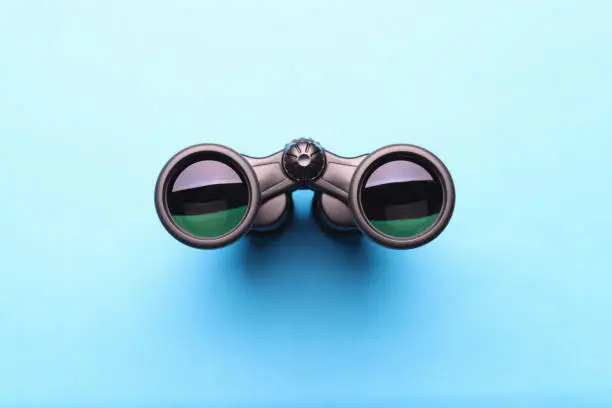 Photo of Black professional binoculars lying on blue background