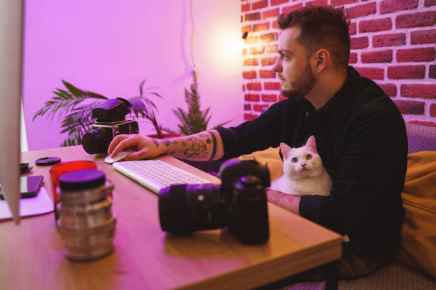 istock Man retouching photos at the computer with his white cat at the laps 1315340090