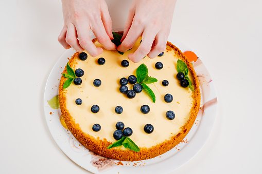 homemade cheesecake hand decorating with blueberry berries and mint leaves. Cooking desserts and cakes. Confectionery.