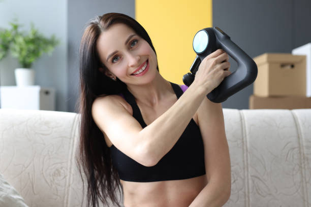 Portrait of young woman with percussion massager in her hands at home Portrait of young woman with percussion massager in her hands at home. Back massage yourself concept percussion instrument stock pictures, royalty-free photos & images