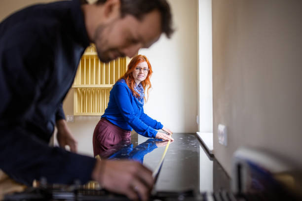 Woman with man measuring granite kitchen counter Redhead woman with man measuring granite kitchen counter. Couple is using tape measure in kitchen. They are examining new apartment. measuring a room stock pictures, royalty-free photos & images