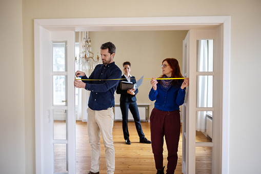 Man and woman measuring doorway with tape. Couple is examining with female Real Estate Agent background. They are at new apartment.