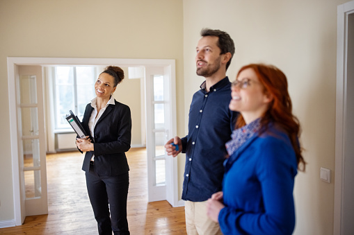 Couple and female Real Estate Agent looking away while standing at empty house. Customers are discussing with real estate agent. They are at new apartment.