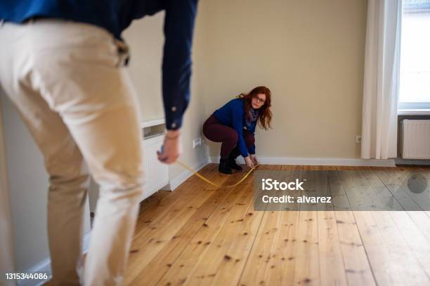 Woman Crouching While Measuring Floor Of New House With Man Stock Photo - Download Image Now