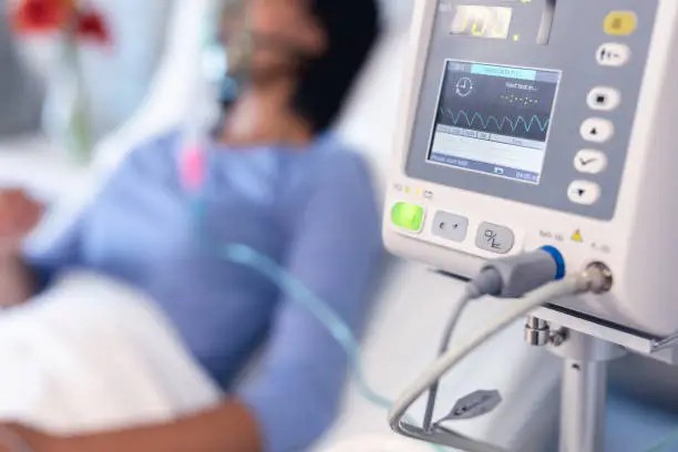 Photo of Ventilator monitor and african american female patient in hospital bed with oxygen ventilator