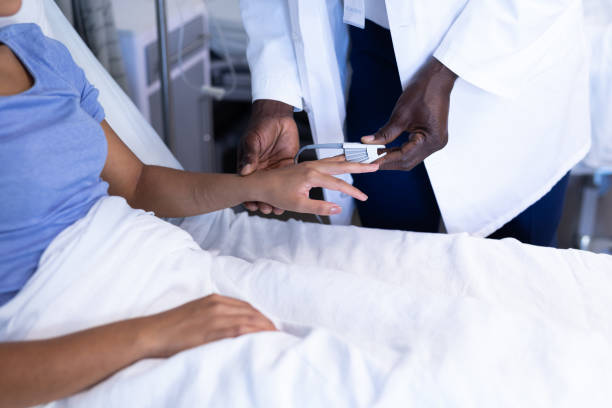 Midsection of african american male doctor putting oximeter on finger of woman in hospital bed Midsection of african american male doctor putting oximeter on finger of woman in hospital bed. medicine, health and healthcare services. pulse oxymeter stock pictures, royalty-free photos & images