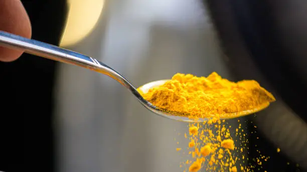 Close-up of turmeric powder falling from a spoon.