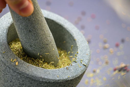 Close-up of dried rosemary leaves being crushed in the mortar with a granite pestle.